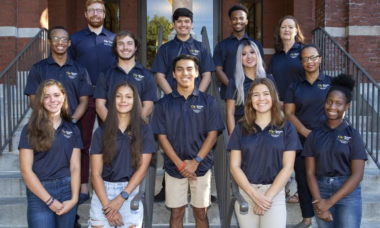 Group photo of 2022 Clark Scholars cohort. Group is dessed in navy blue polo shirts and standing on the front steps of Tech Tower.