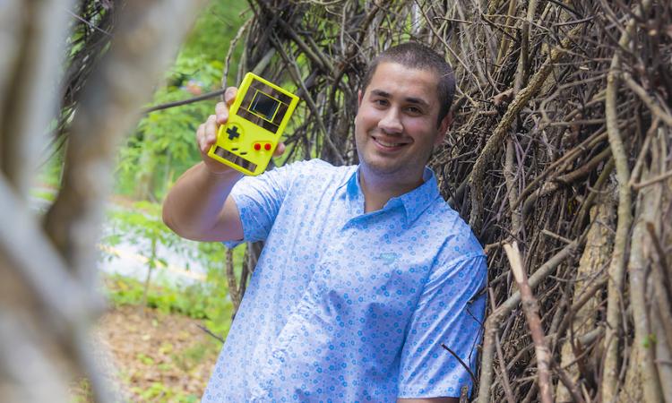 Josiah Hester with a neon yellow device that resembles a Nintendo Game Boy. (Photo: Terence Rushin)