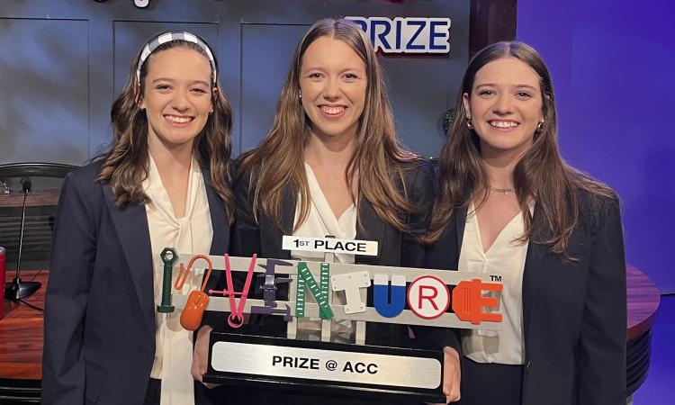 Three women holding the first place trophy at the ACC InVenture Prize competition.