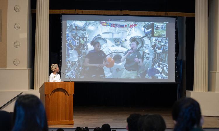 Joy Harris at a podium looking at a large screen with two women astronauts aboard the International Space Station. (Photo: Veronica Soroka)