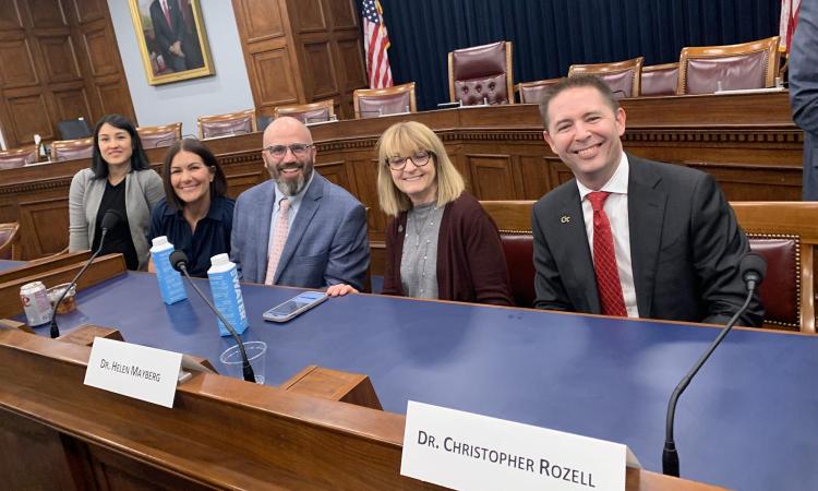 A group of people smiling at a table in a Congressional hearing room.