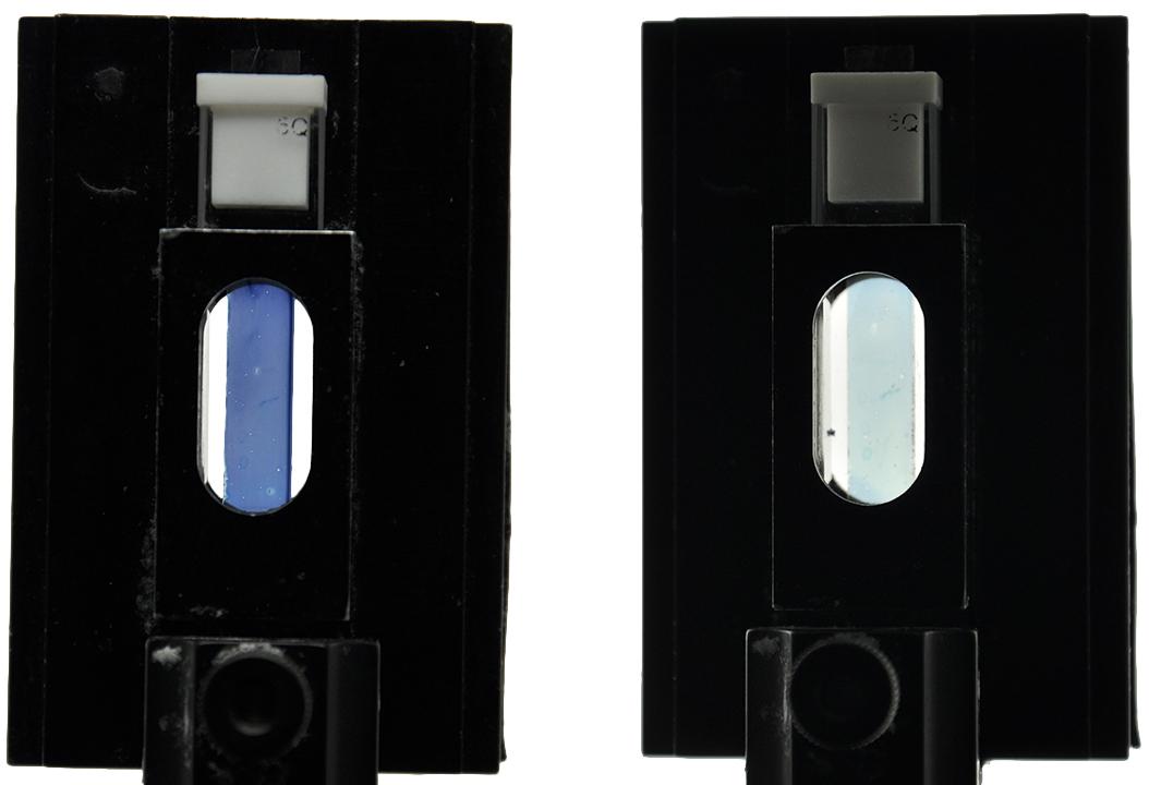 A side-by-side comparison of two black square holders with oval openings in the middle. Inside the oval area of one is a bluish, semi-transparent strip of the PEDOT polymer before the final processing step. The other contians the now-transparent strip of the PEDOT polymer. (Photo Courtesy: James Ponder)