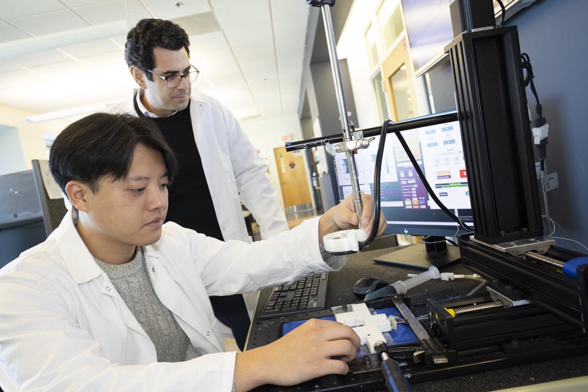 Ph.D. student Hohyun "Henry" Lee adjusts the metal arm holding the ultrasound transducer for his algorithm-controlled focused ultrasound system. Associate Professor Costas Arvanitis looks at data on a computer screen in the background.