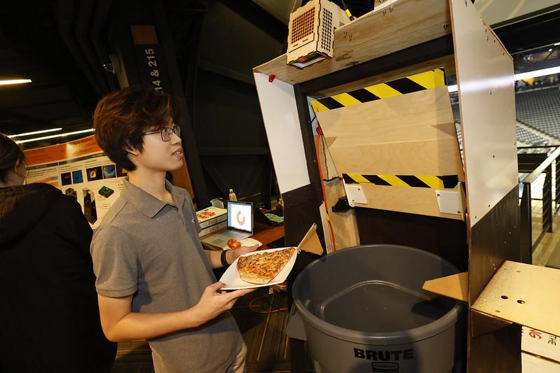 student holding pizza in front of trash can