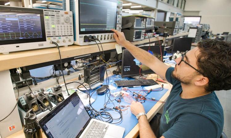 A student uses a laptop and other electronic equipment at a workbench in the Interdisciplinary Design Commons.