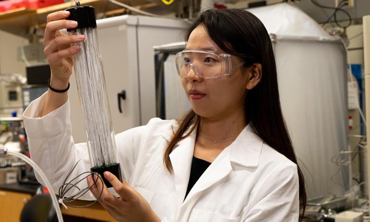 A woman in lab coat and eye protection holds a canister of thin, white sorbent-coated carbon fibers that capture carbon from the atmosphere.