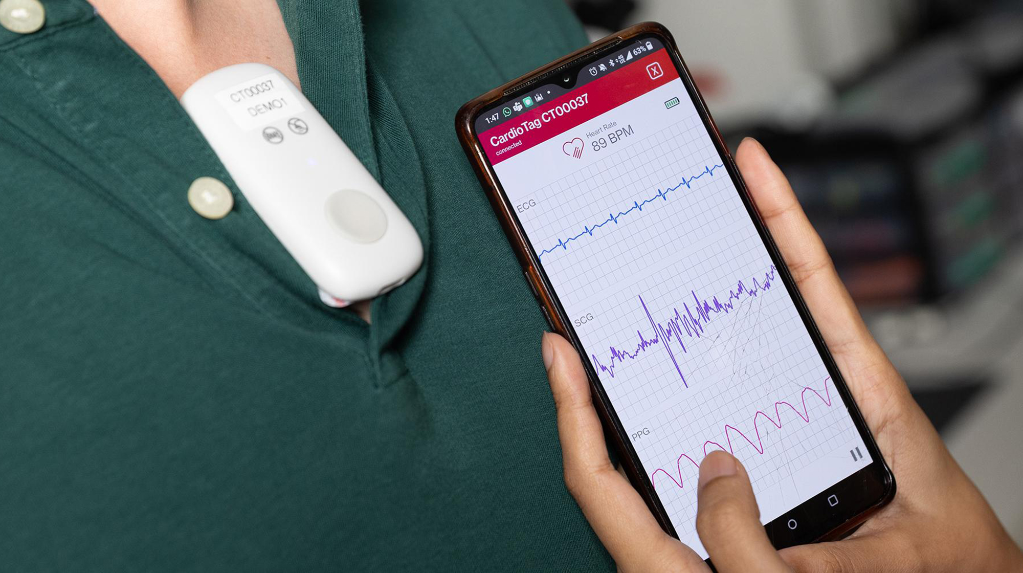 A smartphone displays heart monitoring data from a CardioTag device worn by Ph.D. student Onur Selim Kilic.