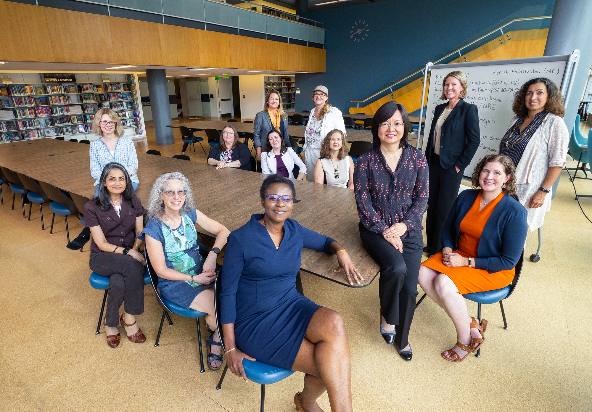 A group picture of 14 women holding leadership positions in the College of Engineering gathered around a table in the library