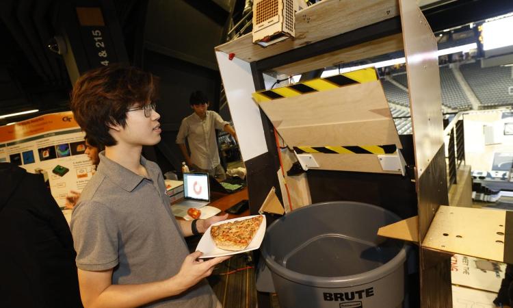 man holding pizza on plate in front of garbage can