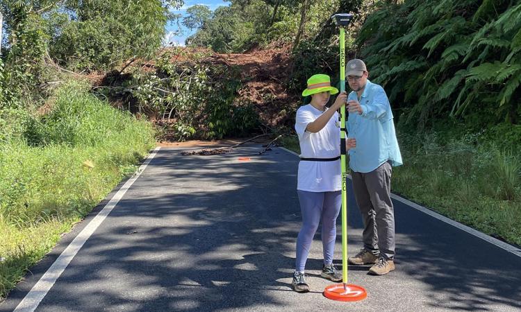 CEE grad student Paola Vargas-Vargas and Stephen Hughes of the University of Puerto Rico, Mayaguez calibrate an instrument on a flourescent yellow pole in front of a landslide. (Photo: Frances Rivera-Hernández)