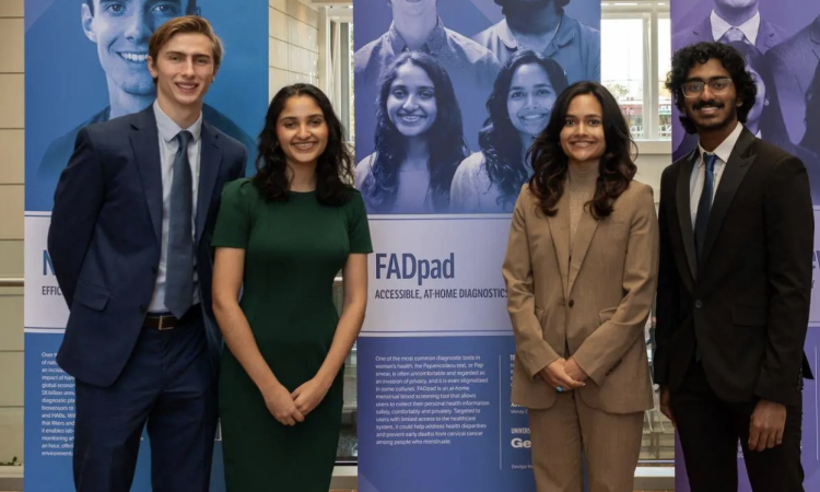 Four students (team fadPAD) stand in front of signage