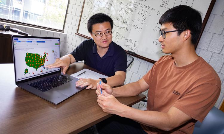 Ph.D student Simin Ma sits with Assistant Professor Shihao Yang at his desk. A computer monitor shows flu data and Google search trends that they used in their Covid and flu forecasting models.