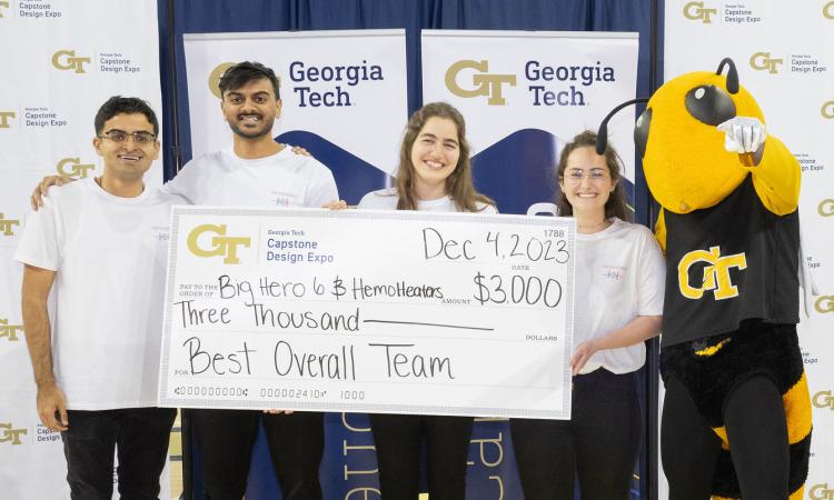 Four students on winning team HemoHeaters pose with Buzz and an oversized check
