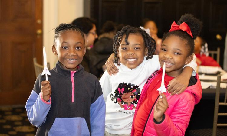 Three young girls arm in arm with big smiles and holding their paper rockets. (Photo: Veronica Soroka)