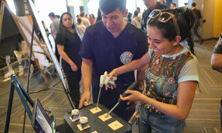 A student smiles while trying out a surgical camera device while a student who designed the tool guides her.