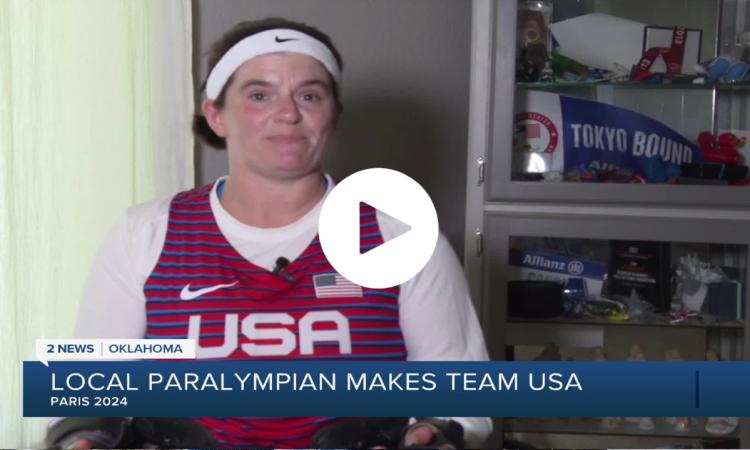 a video still of Cassie Mitchell in a USA jersey with other Paralympic memorabilia behind her