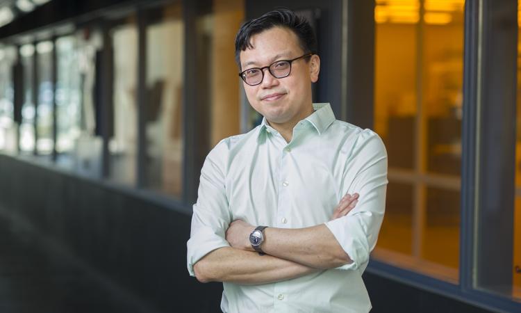 Wilbur Lam stands with his arms crossed in a hallway.