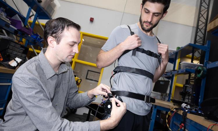 member of team assisting another member putting on a robotic exoskeleton device.