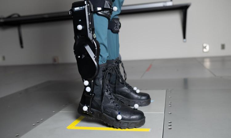 Closeup of ankle exoskeleton boots worn by a person standing on a moveable floor platform.