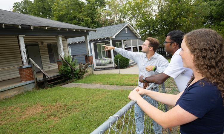 Three people look at a dilapidated house from the front yard