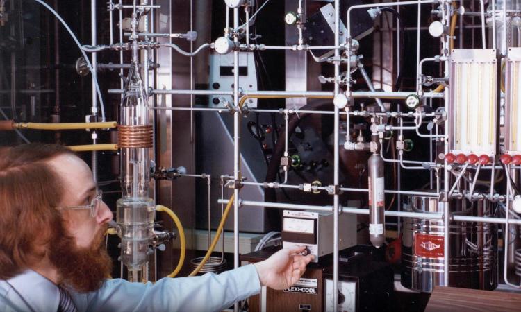 Russell Dupuis sits with a maze of pipes and valves and other equipment that made up his original metal-organic chemical vapor deposition reactor used for making compound semiconductors.