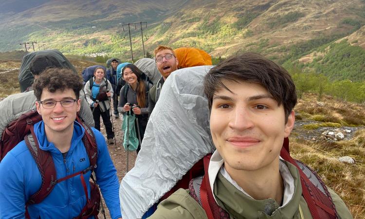 Venny Kojouharov taking a selfie while hiking in Scotland with a group of people on the trail behind him.