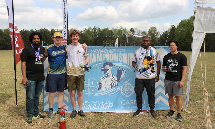 five people with drones in front of a championship banner