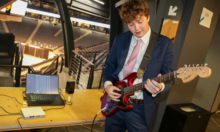 man playing guitar in front of computer screen