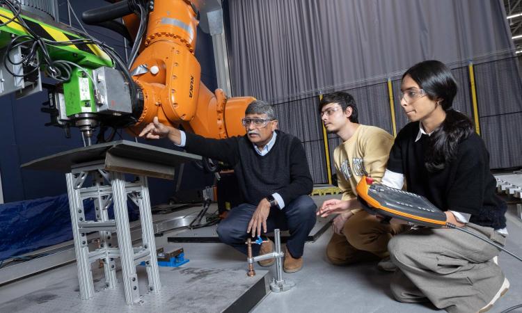 three people squatting with robot arm in background