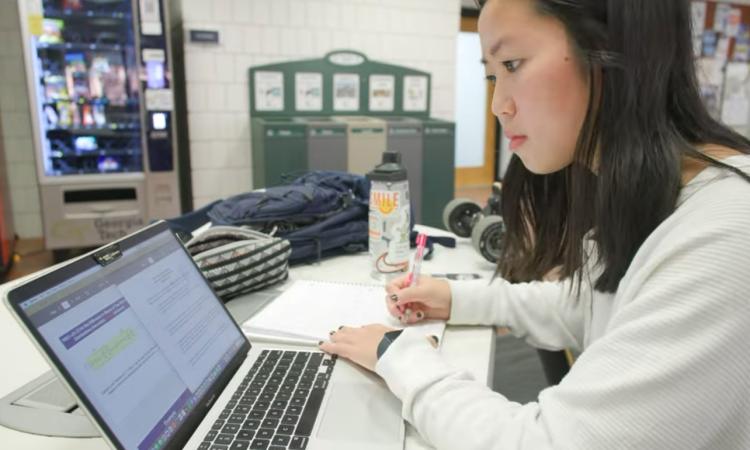 A student taking notes while looking at a laptop