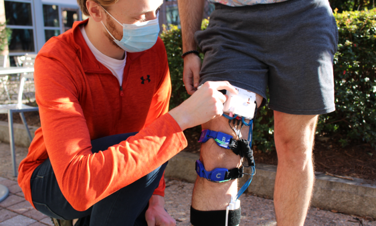 image of researcher helping a participant put on the fully wearable multimodal knee brace for collection of physiological data 