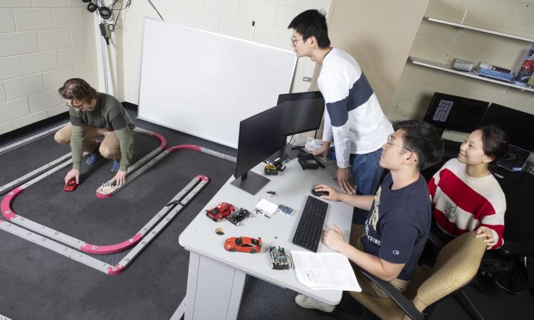 A team of students works with scale model cars on a track to simulate driving scenarios