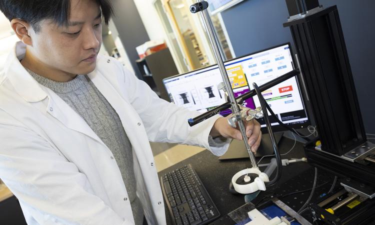 Mechanical engineering Ph.D. student Hohyun “Henry” Lee with the algorithm-controlled focused ultrasound system he developed. Lee is adjusting a metal arm that holds the ultrasound transducer and receiver with a computer behind him displaying information from the control algorithm.