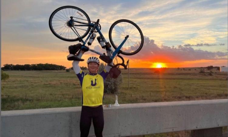 Mjay Choi lifts his bicycle at the Nebraska-Kansas state line with a setting sun in the background.