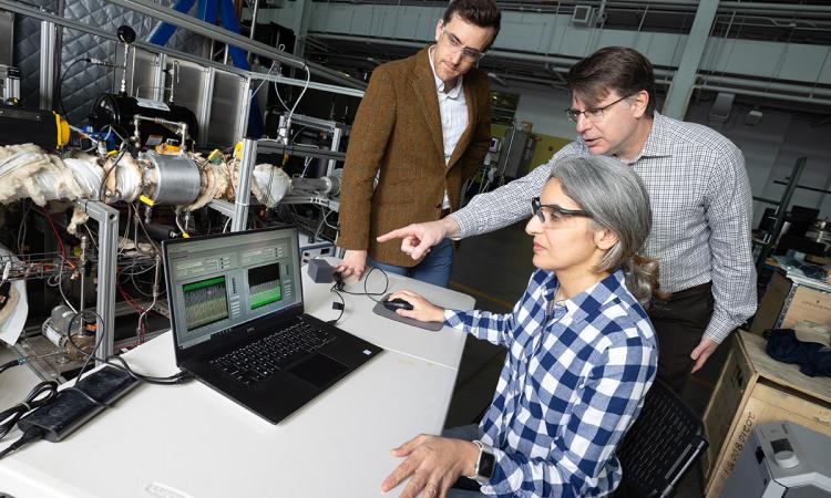 Postdoctoral fellow Poorandokht Kashkouli, seated at laptop, discusses test data from their direct air capture rig. Ryan Lively, left, and Chris Jones, pointing at laptop, stand next to the rig, which is a series of tubes and valves in a metal frame. (Photo: Candler Hobbs)