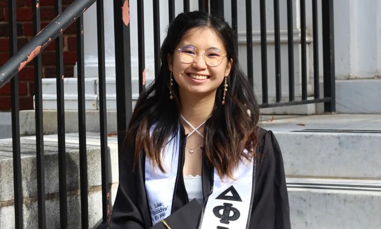 Lisa Wu sits on steps in her cap and gown.