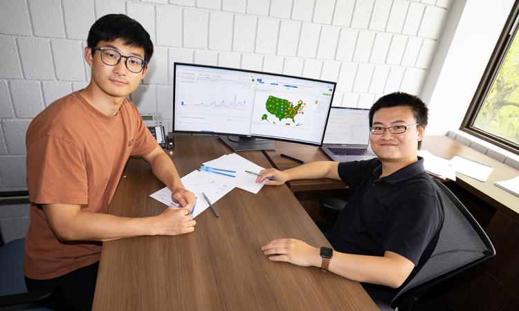Ph.D student Simin Ma sits with Assistant Professor Shihao Yang at his desk. A computer monitor shows flu data and Google search trends that they used in their Covid and flu forecasting models.