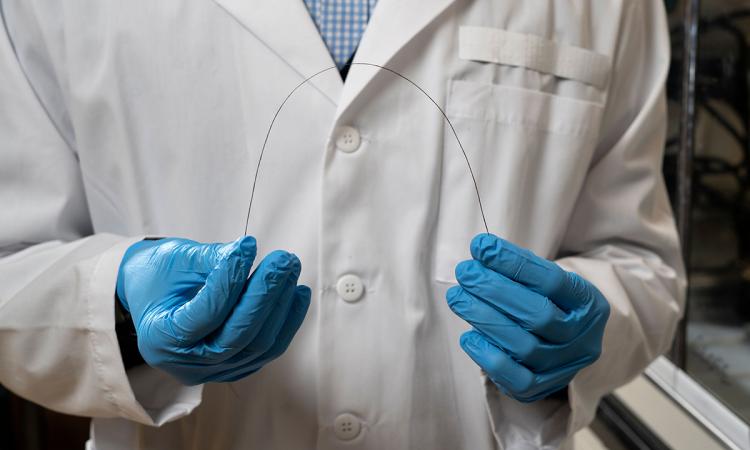 A researcher holds a strand of carbon fiber between two gloved hands.