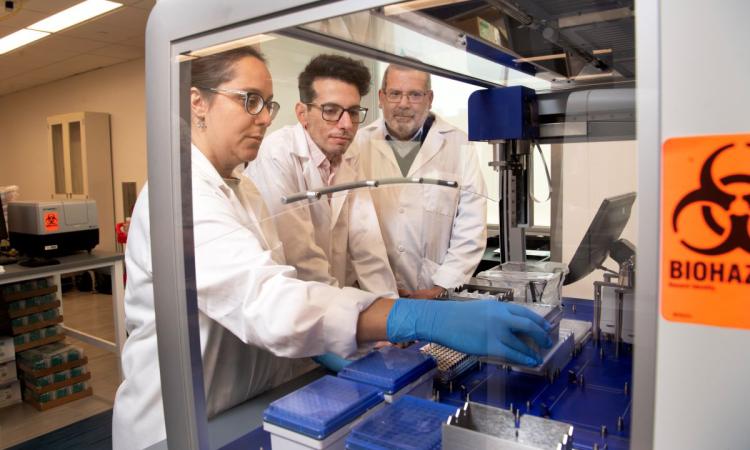 Emory researchers Lorena Chaves, Jose Assumpcao, and Philip Santangelo working at a hood in their lab. (Photo: Jack Kearse)