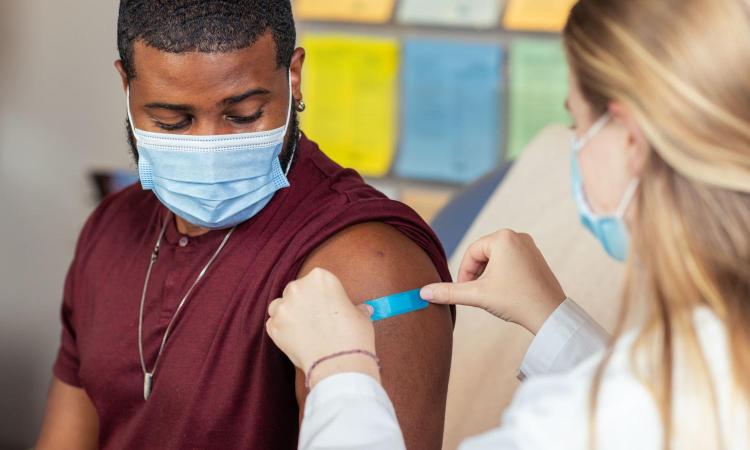 Female nurse puts bandage on arm of male patient after vaccination