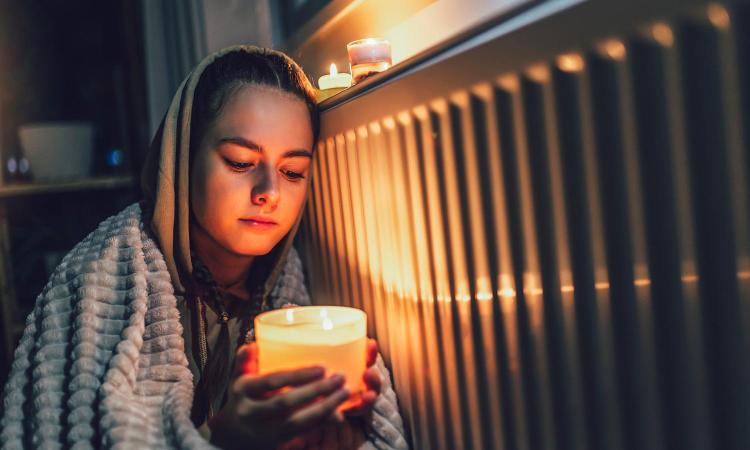 A young girl wrapped in a blanket holds a candle during a power outage.