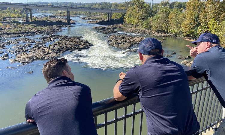 Columbus, Georgia, firefighters on a bridge look out over a section of the Chattahoochee River with rapids and exposed rocks.