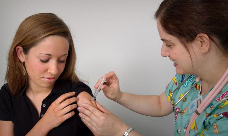 A woman receives an injection in her upper arm from a female nurse.