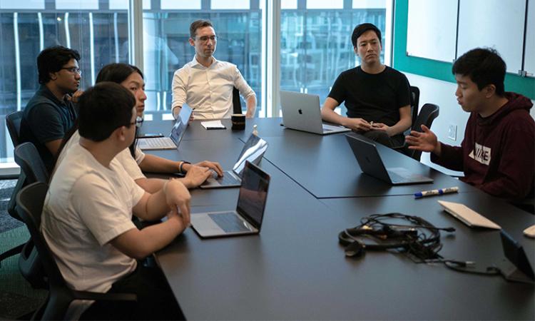 A group of researchers sitting around a table with laptops open.