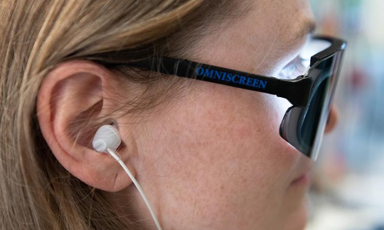 Side view of researcher Annabelle Singer wearing an ear bud and glasses shining a white light on her eyes.