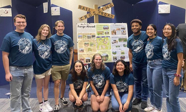 Georgia Tech's 2024 Sustainable Solutions team in group T-shirts pose around their poster and a railroad crossing sign.