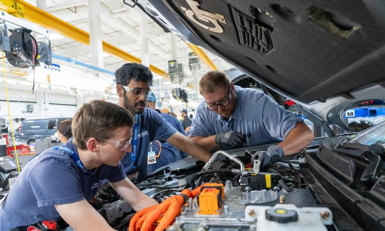 Three people work under the hood of Georgia Tech's EcoCAR, a 2023 Cadillac LYRIQ.