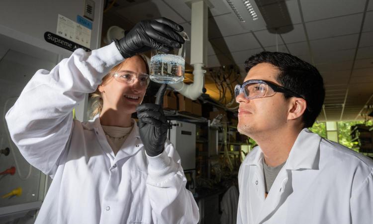 Erik Barbosa and Madeline Morrell examine a beaker of salt beads in a lab.