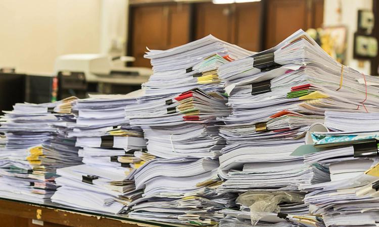 A table with stacks of papers held together with binder clips, rubber bands, and other devices.