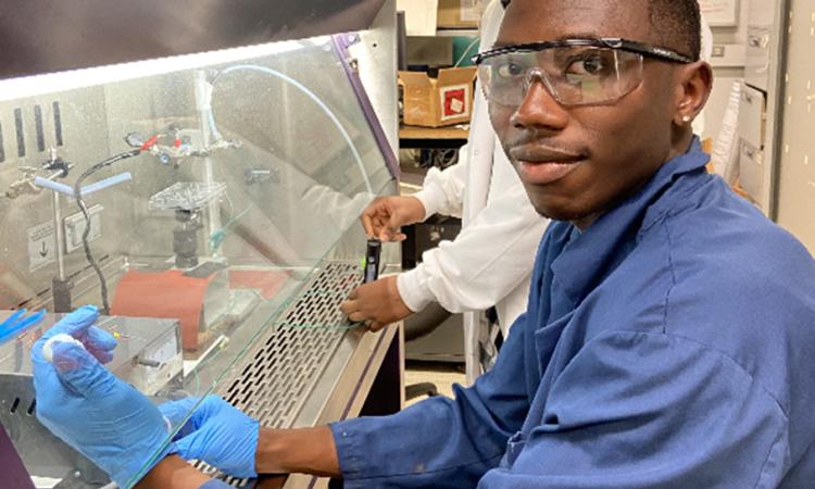 Malik McRae sits at a lab hood conducting experiments with the early prototype of the PAINT device for "direct-write" guided drug delivery to biological cells.